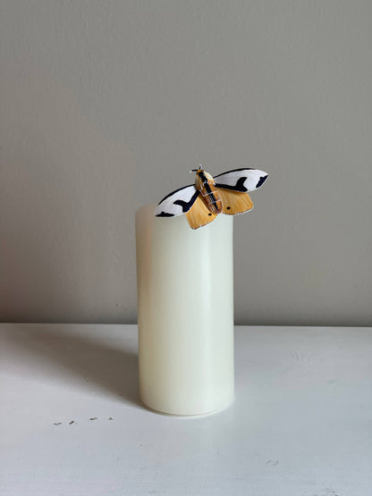 DIY Paper Clymene Moth on a white candle against a plain background