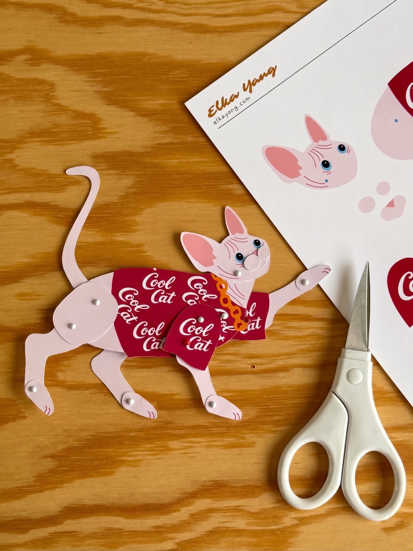 Sphynx in Red Shirt Paper Doll with scissors on a wooden surface.